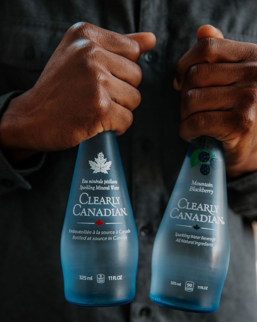 A Clearly Sparkling and a Mountain Blackberry Bottle Each Held in a Hand